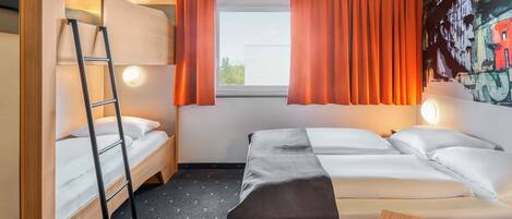 A compact hotel room with two beds, a bunk bed, a ladder, a window with orange curtains, and a wall with a colorful mural.