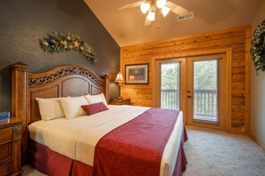 A bedroom with a wooden headboard, a large bed with white and red bedding, a nightstand, a lamp, a framed picture, and a window with blinds.