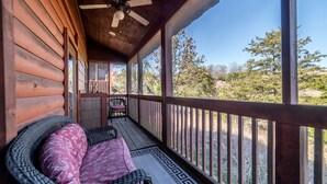 A wooden porch with a ceiling fan, wicker furniture, and a view of the surrounding landscape.