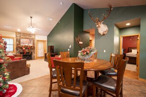 A dining area with a round wooden table and chairs, a Christmas tree, and a mounted deer head on the wall.