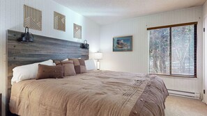 A bedroom with a large bed, a wooden headboard, a painting, and a window with blinds. - Pet Friendly, Bright & Rustic, Walk to Eagle Lodge & Slopes, Complex Hot Tub (Mammoth Lakes)