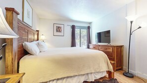 Un dormitorio con cama, cómoda de madera, televisión y ventana con cortinas.