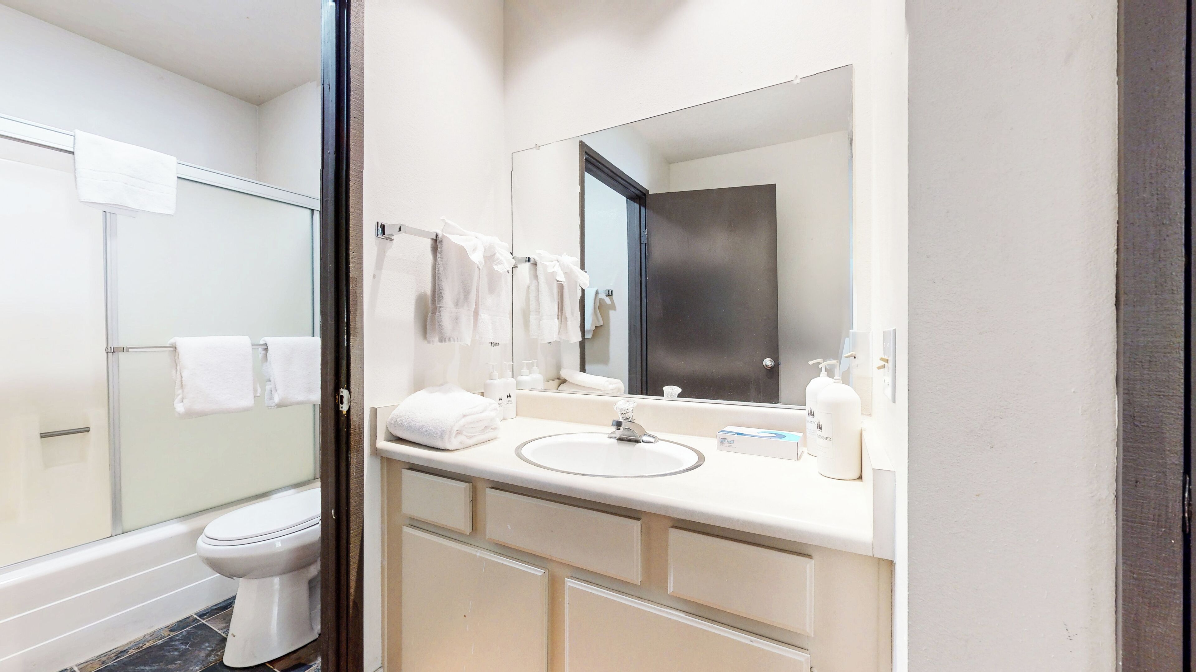 Een moderne badkamer met een douchecabine van glas, een wit toilet, een wastafel met spiegel en keurig opgevouwen handdoeken.