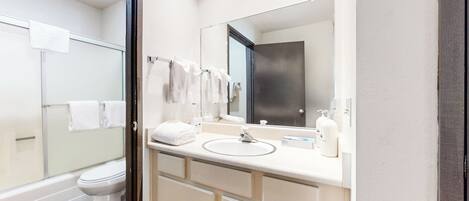 Een moderne badkamer met een douchecabine van glas, een wit toilet, een wastafel met spiegel en keurig opgevouwen handdoeken.