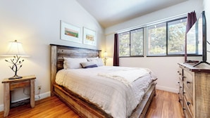A bedroom with a wooden bed, a nightstand with a lamp, a dresser, and a window with curtains. - Remodeled & Spacious, Walk to Eagle Lodge, Slopes & Shuttle, On-Site Hot Tub (Mammoth Lakes)