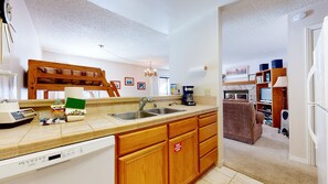 A kitchen with wooden cabinets, a dishwasher, a sink, and a coffee maker. There is a fire extinguisher sign on the cabinet door.