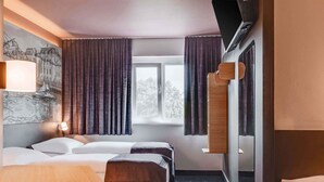 Una habitación de hotel con cama, mesita de noche y ventana con cortinas.