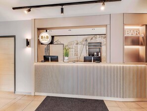 A modern hotel reception desk with a B&B sign, a bar area, and a marble wall with a cityscape mural. - B&B Hotel Oldenburg (Oldenburg)