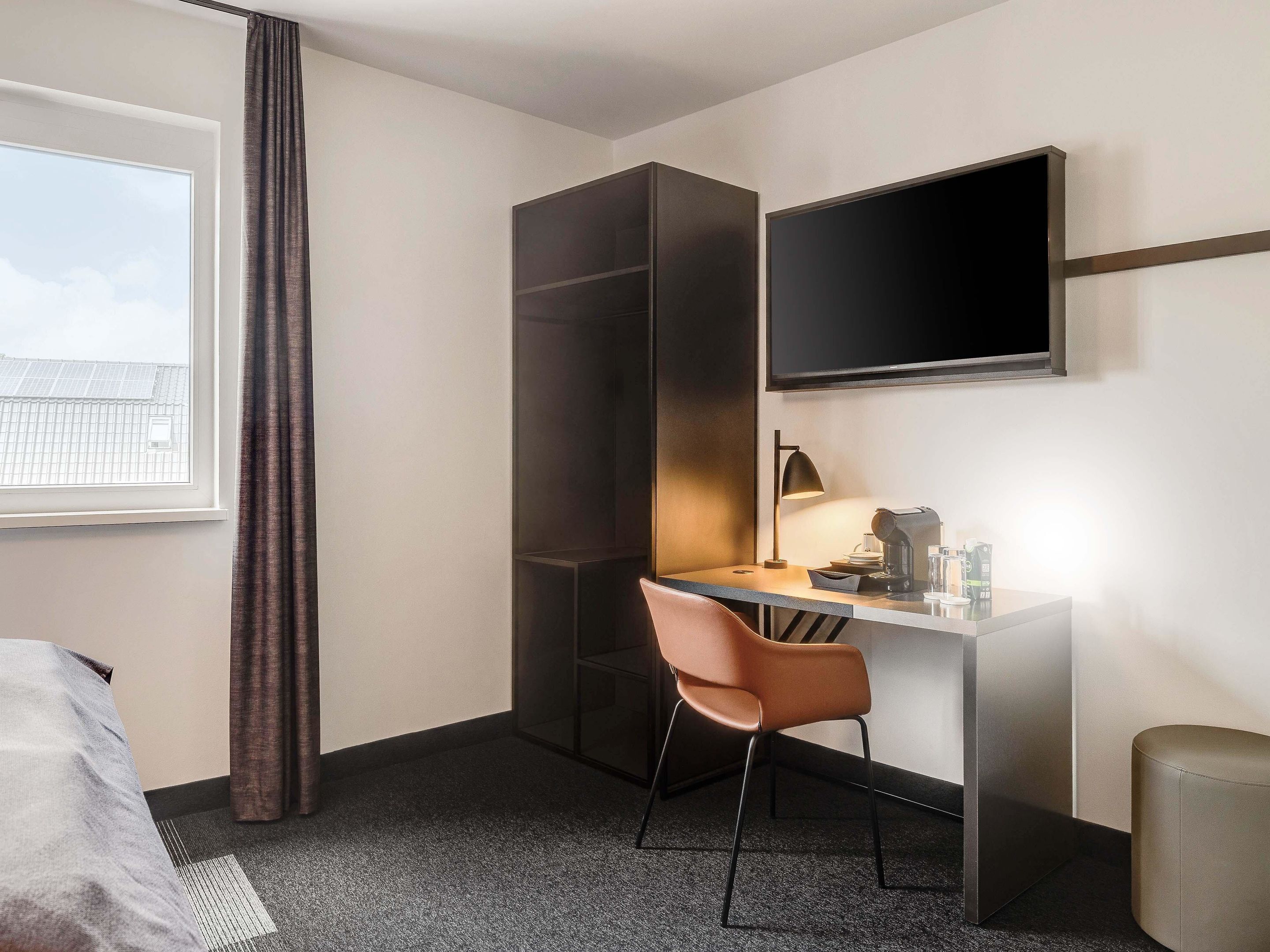 A hotel room with a desk, chair, and a TV mounted on the wall.