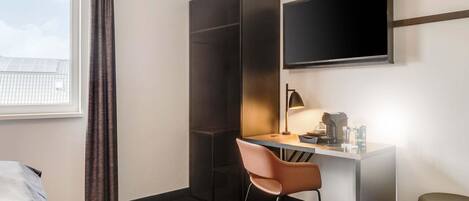 Una habitación de hotel con escritorio, silla y televisor montado en la pared.