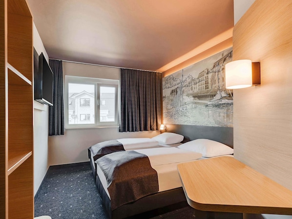 Una habitación de hotel con cama, escritorio, ventana con cortinas, lámpara de pared y un cuadro.