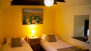A bedroom with two single beds, a nightstand with a lamp, a painting of sunflowers, and a mirror on the wall. - Sunflower Cottage A Cosy, Pet Friendly place to stay. (Huntly)