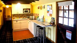 A kitchen with white cabinets, a microwave, a sink, and a bar stool. - Sunflower Cottage A Cosy, Pet Friendly place to stay. (Huntly)