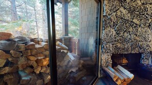 Ein Zimmer mit Kamin, einer Glastür zu einem Außenbereich mit gestapeltem Holz und einer Steinwand.