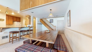 A kitchen with wooden cabinets, a dining table with bench seating, and a staircase leading to an upper level. - Rustic & Large, Private Balcony. Summer Pool, Tennis Courts, Hot Tub On-site (Mammoth Lakes)