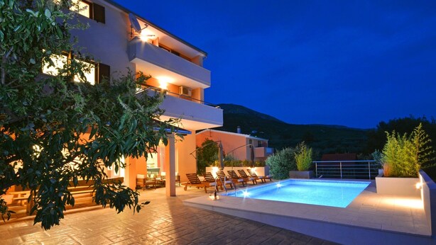A modern building with a swimming pool, outdoor seating, and a mountainous backdrop. - "Villa Karmen Split, Private Garden & Heated Pool (Podstrana)