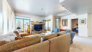Ein geräumiges Wohnzimmer mit Kamin aus Stein, einem großen Flachbildfernseher und einer gemütlichen Sitzecke mit Sofas und einem Sessel.