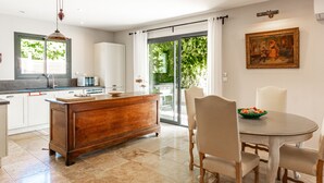 A modern kitchen with a wooden island, a dining area with a round table and chairs, and a large window with a view of greenery.