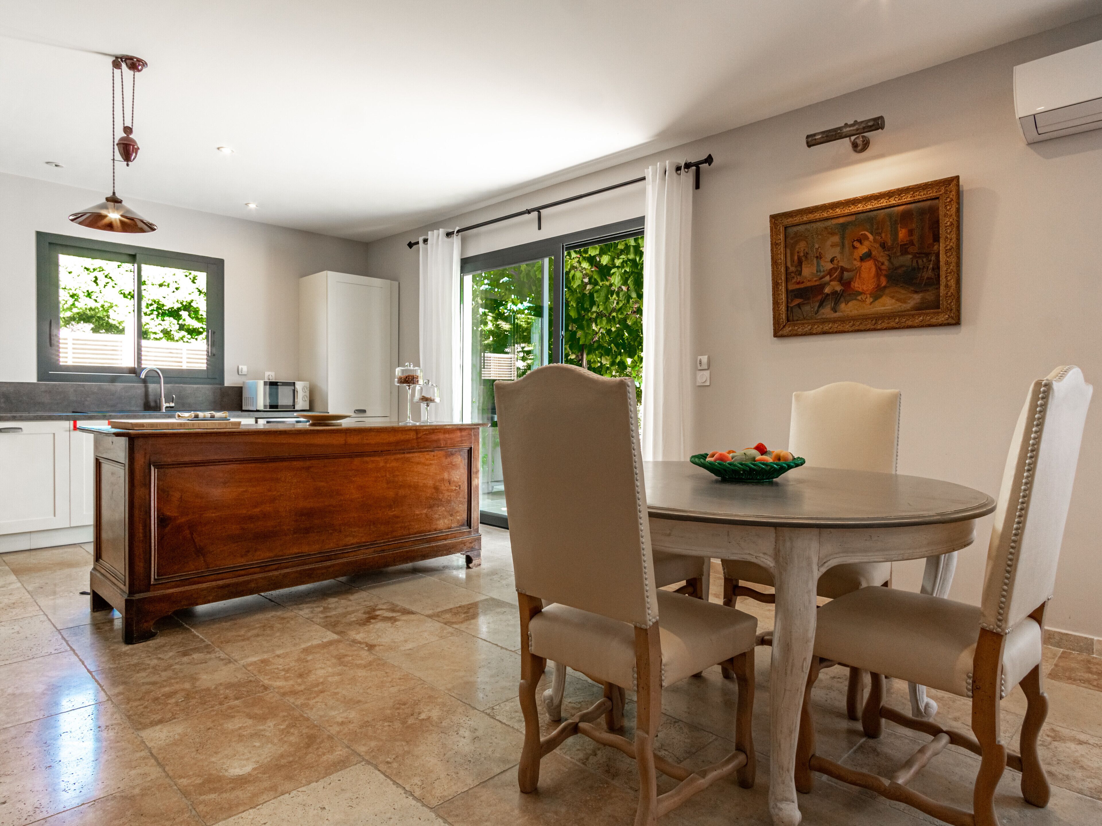 A modern kitchen with a wooden island, a dining table with chairs, and a painting on the wall.