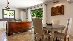 A modern kitchen with a wooden island, a dining table with chairs, and a painting on the wall.