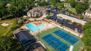 An aerial view of a residential area with a swimming pool, tennis courts, and a covered patio area. - Spacious 3-bedroom golf condo in the scenic Pointe Royale Golf Resort (Branson)