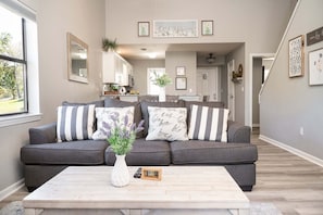 Una sala de estar con un sofá gris, un jarrón blanco con flores y una mesa de centro de madera.