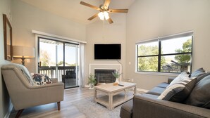 A spacious living room with a fireplace, a ceiling fan, and large windows offering a view of the outdoors. - Spacious 3-bedroom golf condo in the scenic Pointe Royale Golf Resort (Branson)