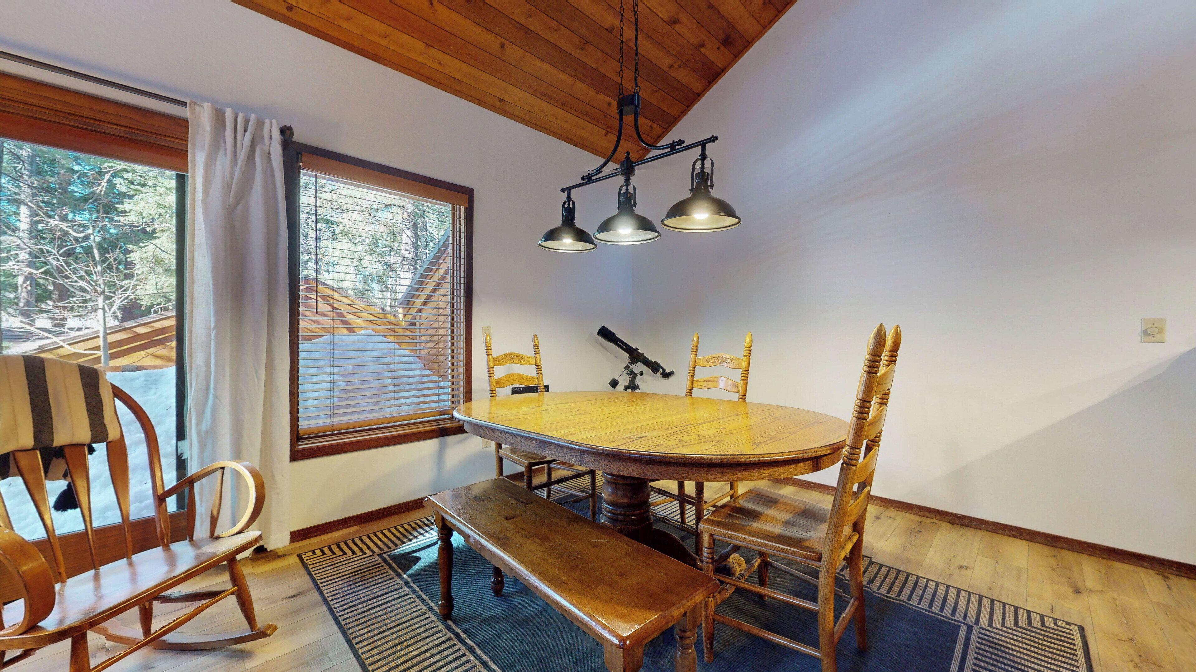Un espace repas comprenant une table en bois, des chaises, un banc et un luminaire suspendu.