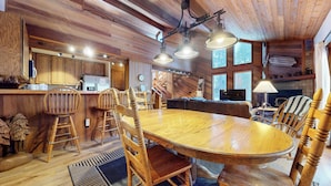 L’intérieur d’un chalet rustique comprend une table à manger en bois, des chaises, un coin cuisine et une cheminée.