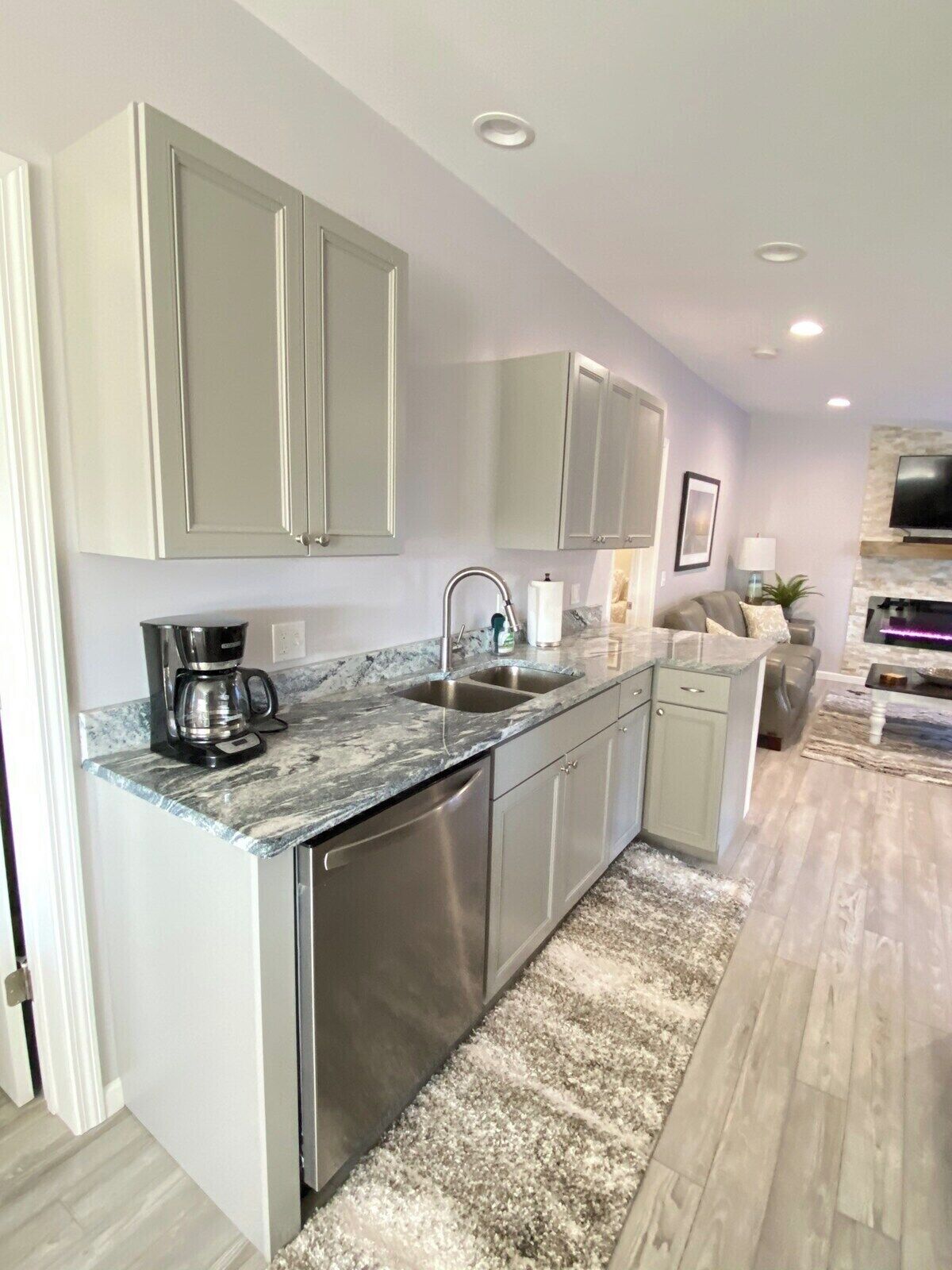A modern kitchen with grey cabinets, a built-in dishwasher, and a marble countertop.