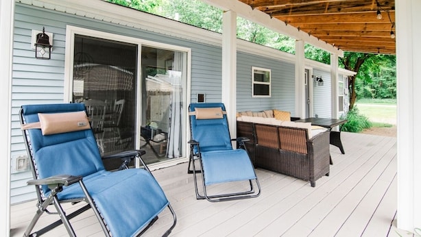 A covered patio with two blue chairs and a wicker table, a sliding glass door, and a wooden ceiling.