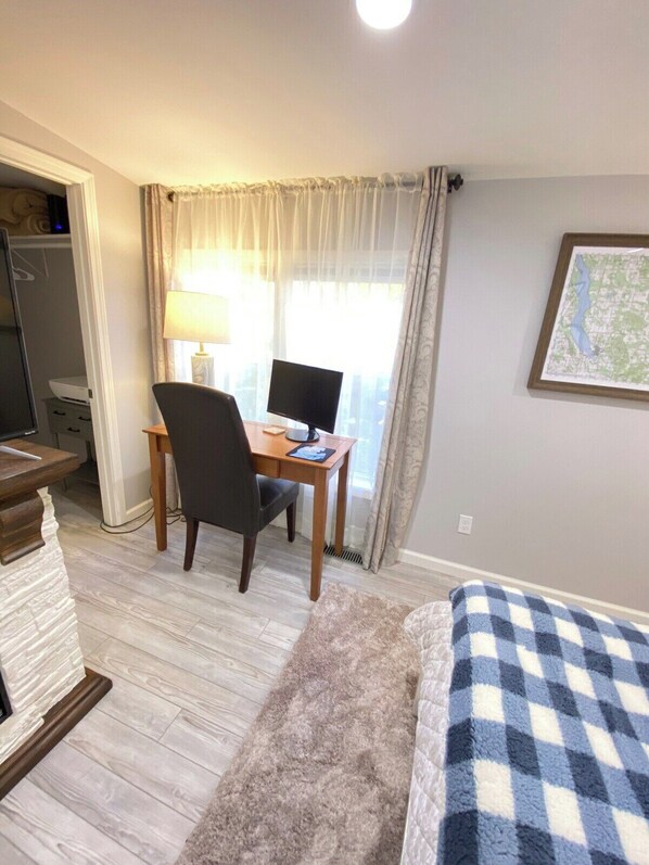 Habitación de hotel con escritorio, silla y computadora, cama con manta a cuadros, y un mapa en la pared.