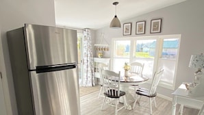 A modern kitchen with a stainless steel refrigerator, white wooden flooring, and a dining area with white chairs and a table.
