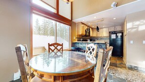 A modern kitchen with wooden cabinets, a black refrigerator, and a dining area with a glass table and wooden chairs. - Spacious & Updated. Across from The Village, Private Balcony & Gas Grill (Mammoth Lakes)