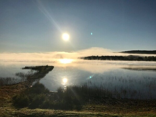 A calm lake with a clear sky and the sun low on the horizon, reflecting on the water's surface. - Direct Trail Access-L & R Lakeside Rentals with this Beautiful Camp on Long Lake (Sinclair)