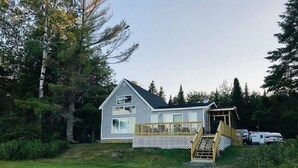 A single-story house with a deck, surrounded by a grassy yard and trees. - Direct Trail Access-L & R Lakeside Rentals with this Beautiful Camp on Long Lake (Sinclair)