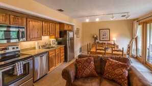 A modern kitchen with stainless steel appliances, wooden cabinets, and a dining area with a table and chairs. - Alpine Condo | 2 Bedroom | Walk to Lifts | Very Convinient (Mt. Crested Butte)