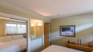 A bedroom with a bed, a bedside table, a mirror, a framed picture on the wall, and a door leading to another room. - Alpine Condo | 2 Bedroom | Walk to Lifts | Very Convinient (Mt. Crested Butte)