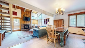 A spacious living room with a fireplace, a dining area with a glass table, and a staircase with wooden railings.
