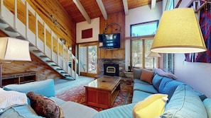A cozy living room with a fireplace, a staircase, and a television.