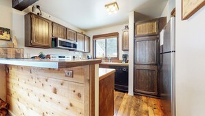 A kitchen with wooden cabinetry, a stainless steel refrigerator, and a central island with a sink. - Spacious Cabin, Rustic Décor. Near Restaurants. Pool & Tennis Court On-site (Mammoth Lakes)