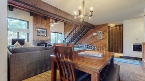 A cozy living room with a wooden dining table, a sofa, and a staircase leading to an upper level. - Large Home, Balcony. Pool & Tennis Court On-site, Short Walk to Restaurants (Mammoth Lakes)