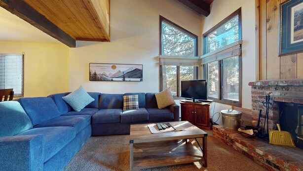 A living room with a blue sectional sofa, a flat-screen TV, a fireplace, and large windows. - Large Home, Balcony. Pool & Tennis Court On-site, Short Walk to Restaurants (Mammoth Lakes)