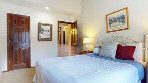 Une chambre d’hôtel avec un grand lit, une porte en bois, un tableau encadré au mur et une table de chevet avec une lampe.