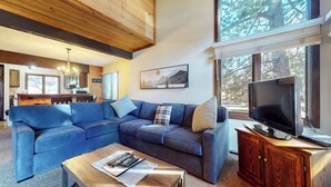 A living room with a sectional sofa, a television, and a wooden cabinet. - Large Home, Balcony. Pool & Tennis Court On-site, Short Walk to Restaurants (Mammoth Lakes)