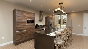 A modern kitchen with a central island, built-in appliances, and a dining area with wooden chairs. - Gorgeous Home! New, Near Disney, Free Parking, Free Wi-Fi Family Friendly Pool (Kissimmee)