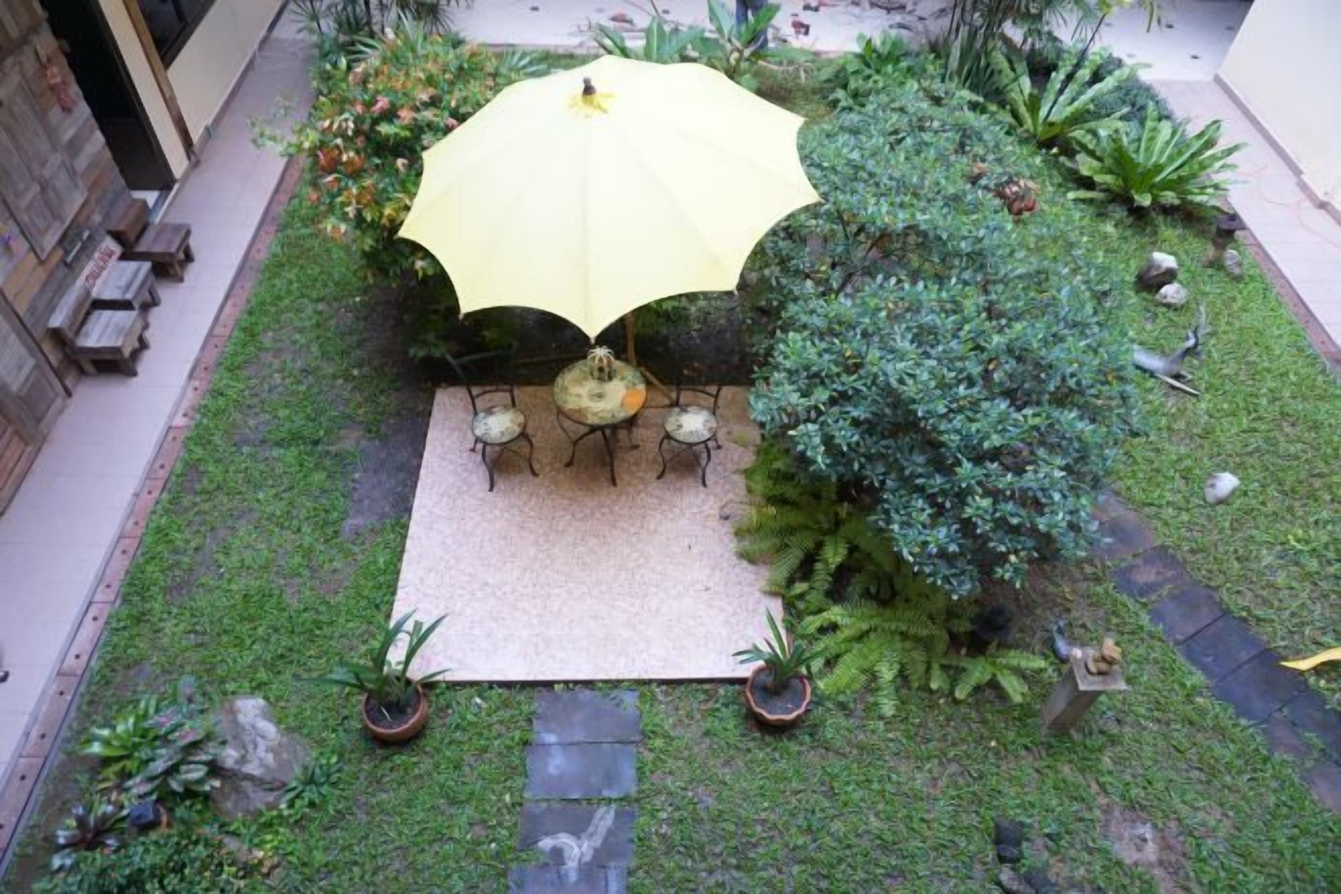Un'area patio con tavolo e sedie sotto un ombrellone giallo, circondata da piante in vaso e un sentiero in pietra.
