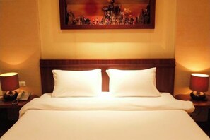 A hotel room with a neatly made bed, two bedside lamps, a telephone on the nightstand, and a painting on the wall.