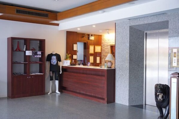 A reception area with a wooden reception desk, a mannequin, a display shelf, and an elevator. - King Hotel (Loei)