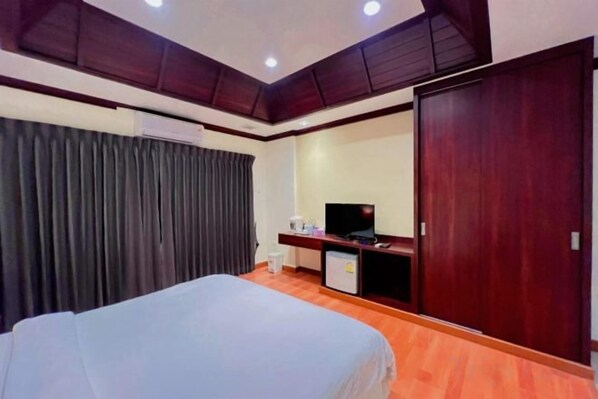 A hotel room with a bed, a desk with a television, a wardrobe, and a window with curtains. - King Hotel (Loei)